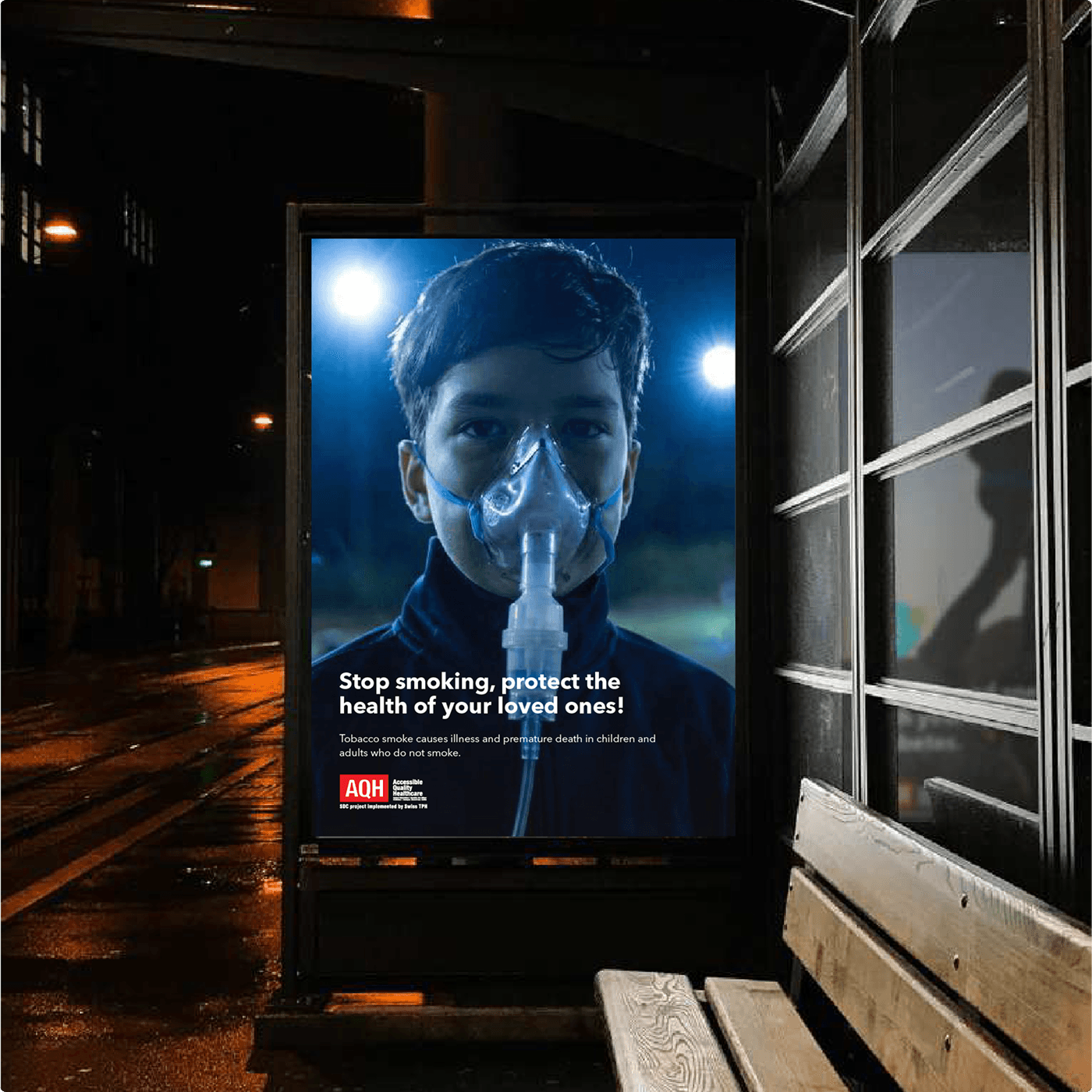 AQH bus shelter poster at night — the same secondhand smoke campaign placed at street level.
