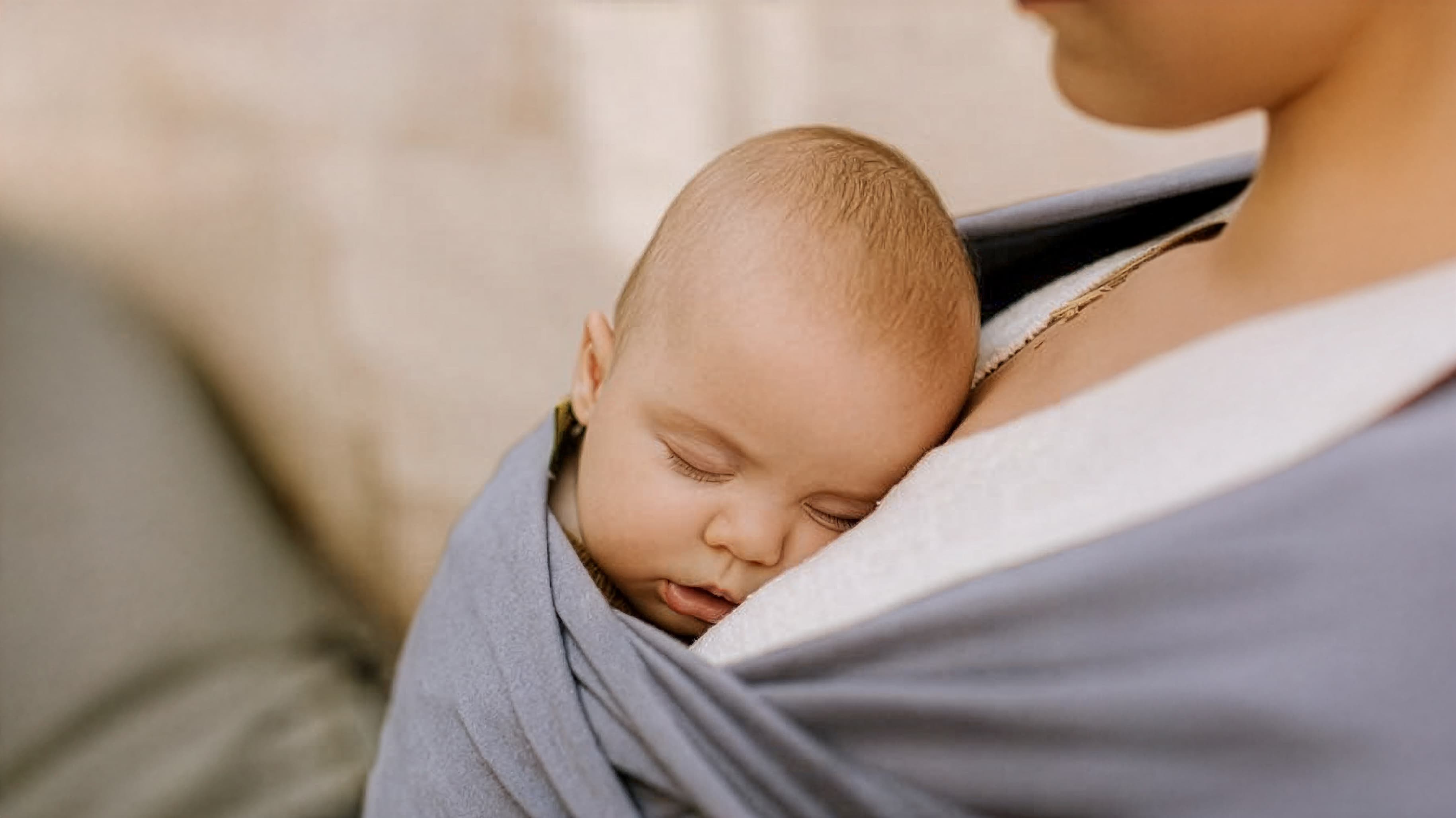 A mother holding a newborn wrapped in a pink Hello Baby Box wrap, with the brand badge visible.